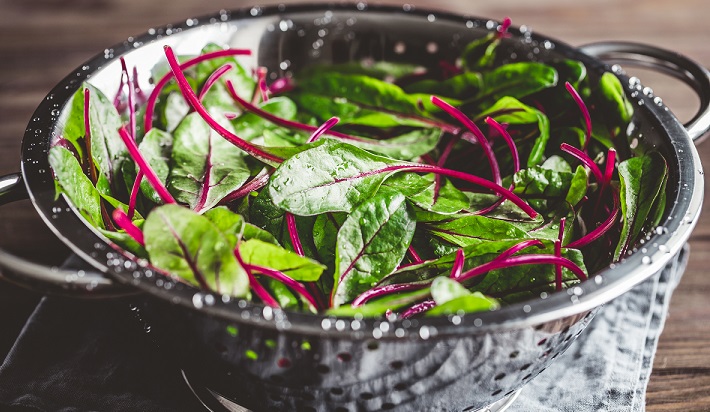 Fresh washed swiss chard leaves in a metal colander on a kitchen table